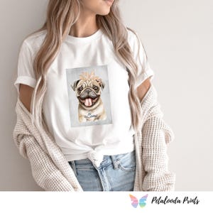 以下が含まれることがあります： 白いTシャツ。水彩画で描かれた、花の冠をつけたパグのイラストが特徴です。パグの名前「Luna」が画像の下に書かれています。このTシャツは、アパレルコレクションの一部です。