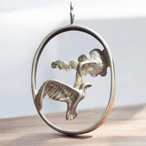 May include: A silver pendant featuring a stylized bird in flight, with a tree branch cut out of the circular design.