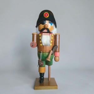 Könnte beinhalten: Eine hölzerne Nussknacker-Figur als Pirat verkleidet, mit einem schwarzen Hut samt rot-gelbem Emblem, einer schwarzen Augenklappe, einem weißen Kunstfellbart, einer braunen Jacke mit gelben Knöpfen, grüner Hose, einem Holzbein und einem kleinen braunen Beutel.