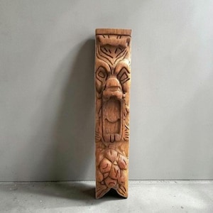May include: A vertical wooden corbel featuring a hand-carved design of a roaring creature with an open mouth at the center, topped with geometric patterns and finished with a cluster of carved fruit or floral elements at the bottom base.