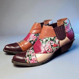 May include: A pair of patchwork ankle boots. The boots feature a mix of leather panels in brown, burgundy, and tan, accented with floral fabric inserts. The heels are a dark brown color.