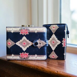 May include: Two vintage black wallets with ornate gold and red designs. The wallets have a square shape with a clasp closure. The design includes diamond and floral patterns. One wallet has a button closure.