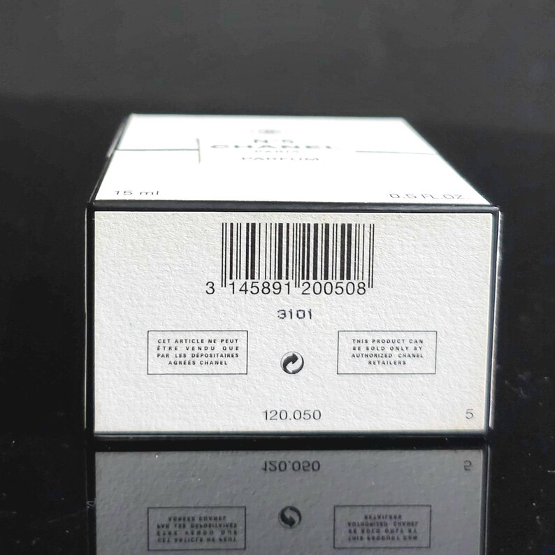 May include: A white rectangular box with black text and a barcode. The box has the text "CHANEL" and "N&deg;5 PARFUM" printed on it. The box also has the text "15 ml" and "0.5 FL. OZ."