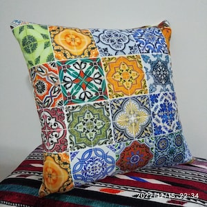 Peut inclure: Un coussin décoratif coloré avec un motif patchwork composé de différents motifs géométriques dans des tons de bleu, vert, jaune, orange et rouge. Le coussin est en tissu et a une forme carrée.