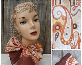 May include: A vintage scarf featuring a paisley design in brown, orange, and white is displayed on a mannequin head. The scarf is tied in a bow. Additional images show the scarf's pattern and a folded scarf.