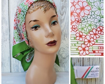 May include: A green, white, and red patterned silk scarf with a floral design. The scarf is tied around a mannequin's head. The label on the scarf reads "100% Polyester, WPL 209, Made in Italy."