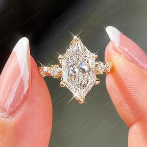 Puede incluir: Un anillo de oro con una gran piedra central de talla marquesa con una superficie facetada brillante. La banda está acentuada con piedras más pequeñas de talla redonda a los lados, creando un aspecto brillante con acabado en oro amarillo.
