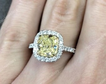 May include: A yellow cushion-cut diamond engagement ring with a halo setting. The ring is set in white gold and features a double row of smaller diamonds around the center stone.