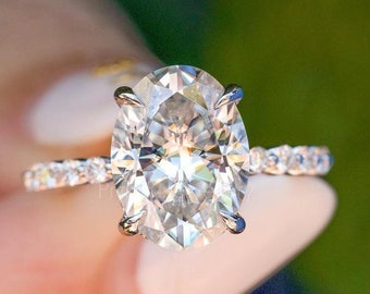 Könnte beinhalten: Ein silberner Ring mit einem großen ovalen Diamanten, der in einer Krappenfassung sitzt. Die Ringschiene ist mit kleineren Diamanten besetzt.