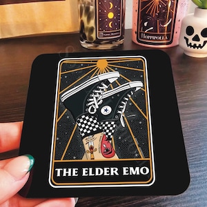 May include: A black and gold tarot card with a black background and gold accents. The card features a pair of black and white checkered Converse sneakers with a red eye and a dagger on the ankle. The card is titled "The Elder Emo".