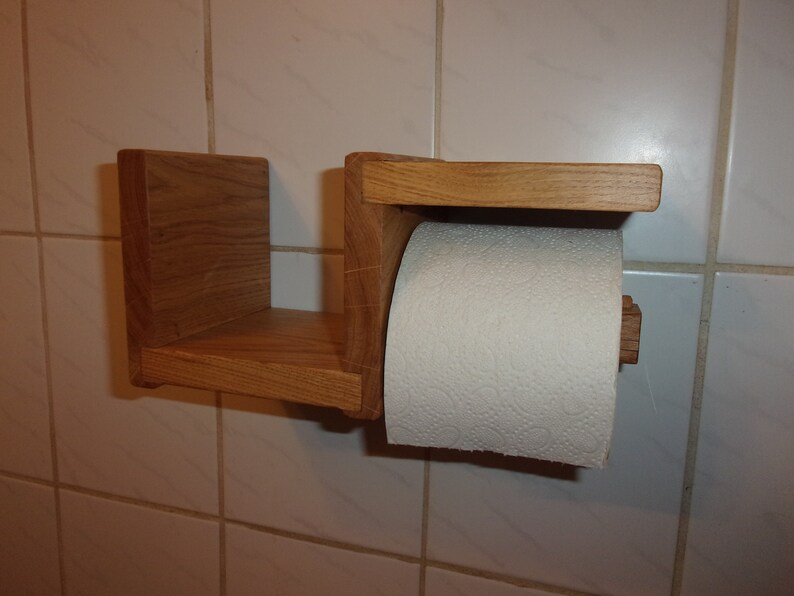 K&ouml;nnte beinhalten: Ein Toilettenpapierhalter aus Holz mit einem Regal. Der Halter ist aus hellbraunem Holz gefertigt und hat ein schlichtes Design. Das Regal ist perfekt, um kleine Gegenst&auml;nde wie Handt&uuml;cher oder Seife zu verstauen.