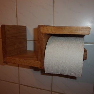 K&ouml;nnte beinhalten: Ein Toilettenpapierhalter aus Holz mit einem Regal. Der Halter ist aus hellbraunem Holz und hat ein schlichtes Design. Eine Rolle wei&szlig;es Toilettenpapier befindet sich auf dem Halter.