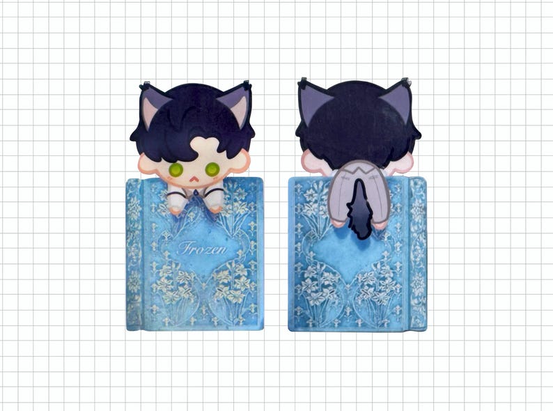 May include: A blue bookmark featuring a cartoon character with cat ears, perched on a book. The book has a floral design and the word "Frozen" on the cover. The character has dark hair, green eyes, and is wearing a white outfit.