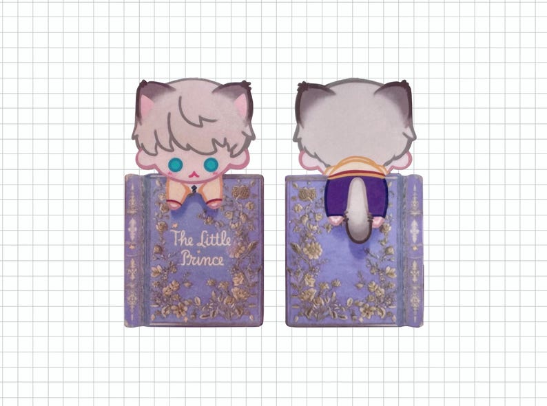 May include: A whimsical bookmark featuring a cartoon cat character with light gray fur and blue eyes, perched atop a purple book. The book is adorned with floral designs and the title "The Little Prince".