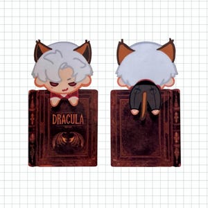 May include: A Dracula-themed bookmark featuring a cartoon character with white hair, brown ears, and a red shirt, perched on a book. The book is dark red with the title "DRACULA" and a bat illustration.