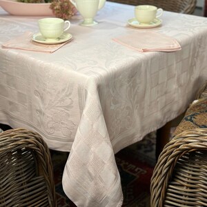 May include: A pink damask tablecloth with a delicate floral pattern. The tablecloth is draped over a table with two chairs and a teapot and cups.