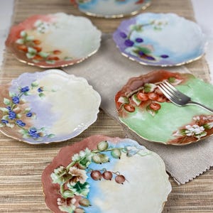 May include: Set of six vintage porcelain dessert plates with hand-painted floral designs featuring various fruits, including berries, cherries, and currants. The plates have a scalloped edge and are trimmed in gold.