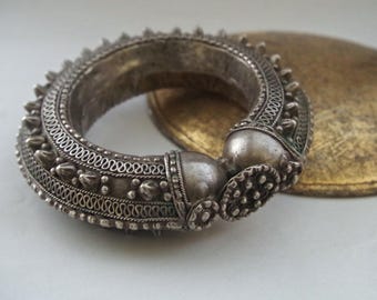 May include: A silver bangle bracelet with intricate designs and a beaded texture. The bracelet is made of metal and has a circular shape.