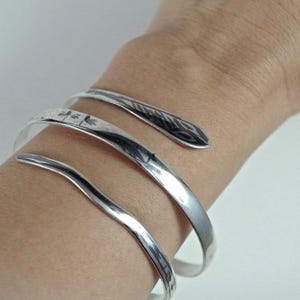 May include: A silver bracelet with a unique, twisted design. The bracelet is made of three separate bands that are intertwined.