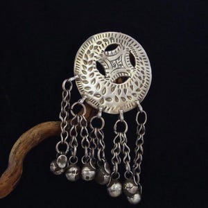 Peut inclure: Une ornement de cheveux en argent avec un motif circulaire et des chaînes pendantes avec de petites cloches. L'ornement est fixé à un bâton en bois.