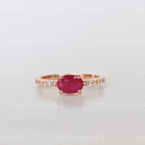 K&ouml;nnte beinhalten: Ein Ring aus Ros&eacute;gold mit einem roten ovalen Rubin und einer Reihe kleiner Diamanten.