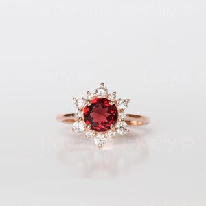 Könnte beinhalten: Ein Ring aus Roségold mit einem großen roten Edelstein, der von kleineren klaren Edelsteinen umgeben ist.