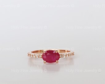 May include: A rose gold ring featuring a red oval ruby gemstone and a band of small diamonds.