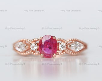 Könnte beinhalten: Ein Ring aus Roségold mit einem großen ovalen Rubin, der von kleineren Diamanten umgeben ist. Der Ring hat ein zartes, filigranes Design.