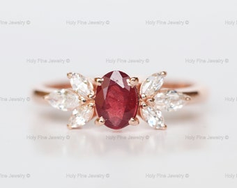 May include: A rose gold ring with a large oval ruby gemstone surrounded by smaller white diamonds set in a leaf-like design.