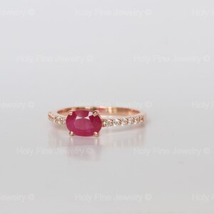 K&ouml;nnte beinhalten: Ein Ring aus Ros&eacute;gold mit einem roten ovalen Rubin und einer Reihe kleiner Diamanten.