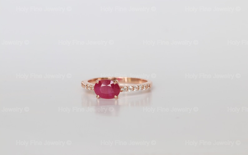 K&ouml;nnte beinhalten: Ein Ring aus Ros&eacute;gold mit einem roten ovalen Rubin und einer Reihe kleiner Diamanten.