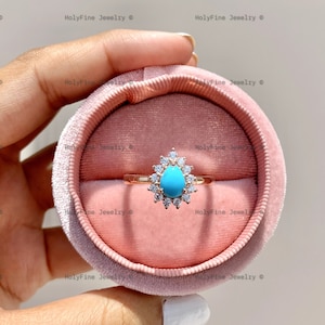 May include: A turquoise gemstone ring with a pear-shaped stone surrounded by a halo of smaller clear stones. The ring is set in a rose gold band and is displayed in a pink velvet ring box.