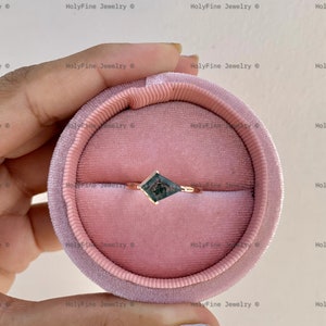 May include: A rose gold ring with a square-shaped green gemstone set in a prong setting. The ring is displayed in a pink velvet ring box.