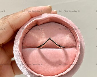 May include: A delicate ring with a V-shaped design set with black diamonds. The ring is displayed in a pink velvet ring box.