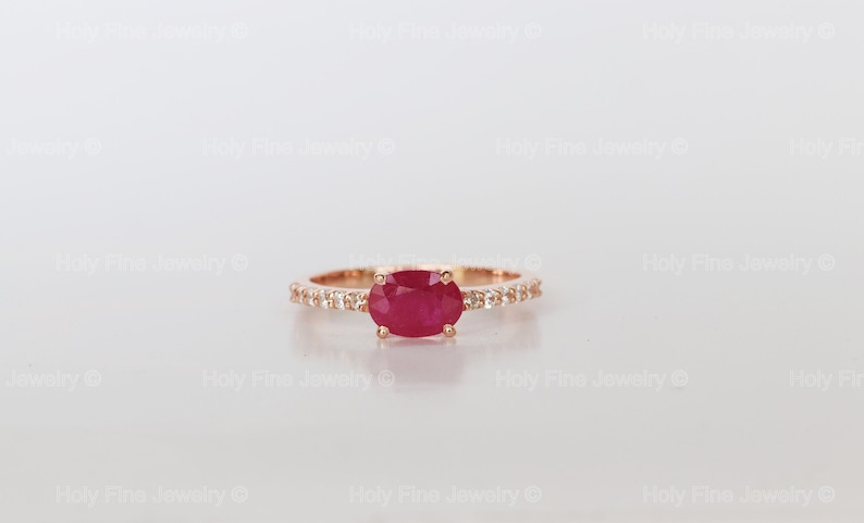 K&ouml;nnte beinhalten: Ein Ring aus Ros&eacute;gold mit einem roten ovalen Rubin und einer Reihe kleiner Diamanten.