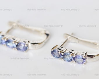 May include: A pair of silver hoop earrings with three oval-shaped blue gemstones. The earrings have a hinged closure.