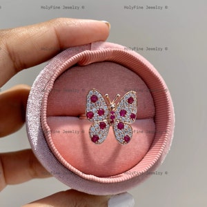 May include: A pink velvet ring box with a butterfly ring inside. The butterfly is made of gold and has red and white stones.