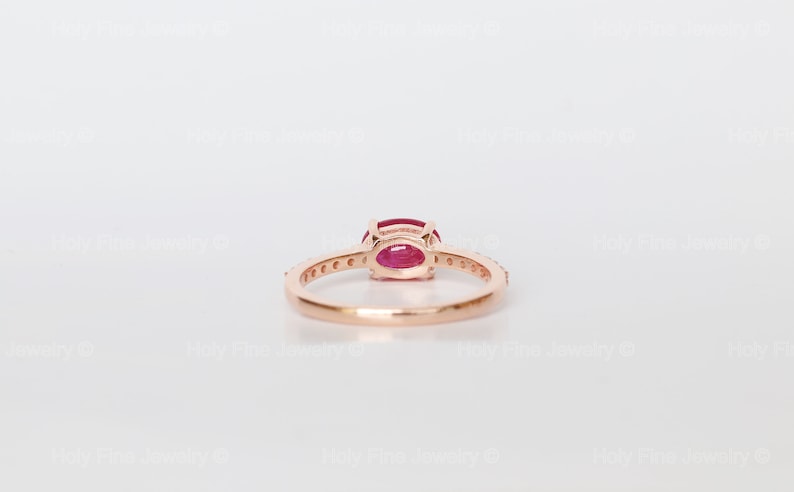 K&ouml;nnte beinhalten: Ein Ring aus Ros&eacute;gold mit einem roten ovalen Edelstein und einer Reihe kleiner Diamanten.