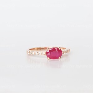 K&ouml;nnte beinhalten: Ein Ring aus Ros&eacute;gold mit einem roten ovalen Rubin und einer Reihe kleiner, klarer Diamanten.