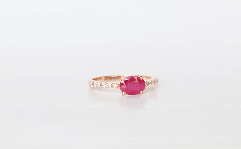 K&ouml;nnte beinhalten: Ein Ring aus Ros&eacute;gold mit einem roten ovalen Rubin und einer Reihe kleiner, klarer Diamanten.