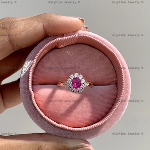 Peut inclure: Une bague en or rose avec une pierre précieuse rose entourée de petites pierres blanches. La bague est dans un écrin à bague en velours rose.