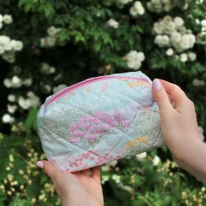 May include: A quilted makeup bag with a floral print in shades of pink, green and yellow. The bag has a pink zipper.