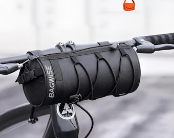 May include: A black cylindrical bicycle handlebar bag featuring the text BAGWISE printed vertically on the side. The bag includes a top zipper closure, adjustable straps for mounting, and a black elastic cord lacing system on the front exterior.