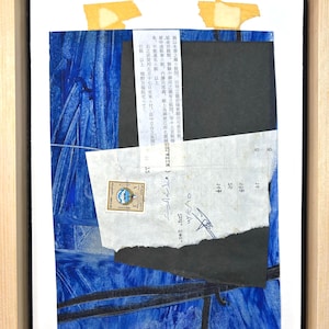 May include: Abstract mixed media artwork in a wooden frame. The artwork features a blue background with layered paper elements, including a stamp and text fragments. The composition is a collage of textures and colors.