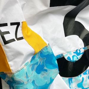 May include: A white jacket with a yellow and blue camouflage pattern. The jacket has a black patch with the word "EZ" on it.