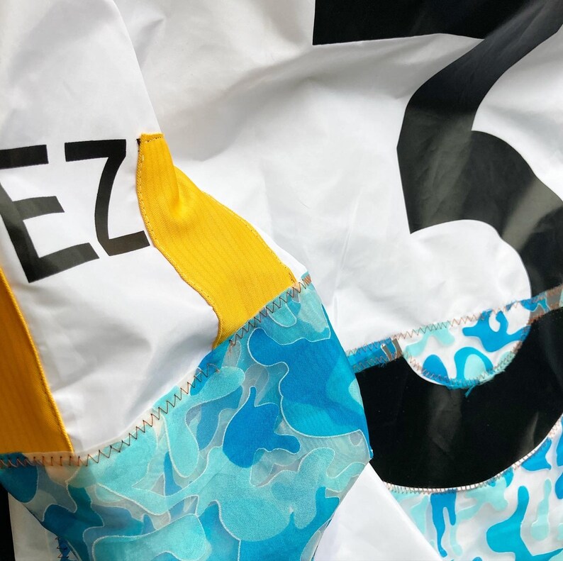 May include: A white jacket with a yellow and blue camouflage pattern. The jacket has a black patch with the word "EZ" on it.