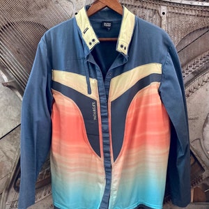 May include: A blue jacket with a color gradient design in orange, yellow, and blue. The jacket has a light yellow collar and accents, with the text "SUPERFREAK" on the front. The brand name "EILEEN FISHER" is visible on the collar.