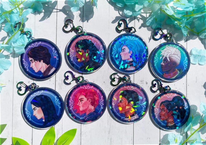 May include: Eight iridescent round keychains with different character illustrations. Each keychain features a different character with a unique design and color scheme. The keychains are made of clear acrylic with a holographic finish.
