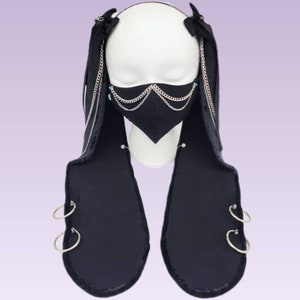 May include: Black face mask with silver chains and blue accents. The mask is attached to two long black fabric strips with silver rings.