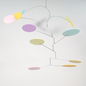 Puede incluir: Un móvil colorido con círculos pastel rosa, amarillo, azul claro y verde colgando de un marco de alambre plateado.